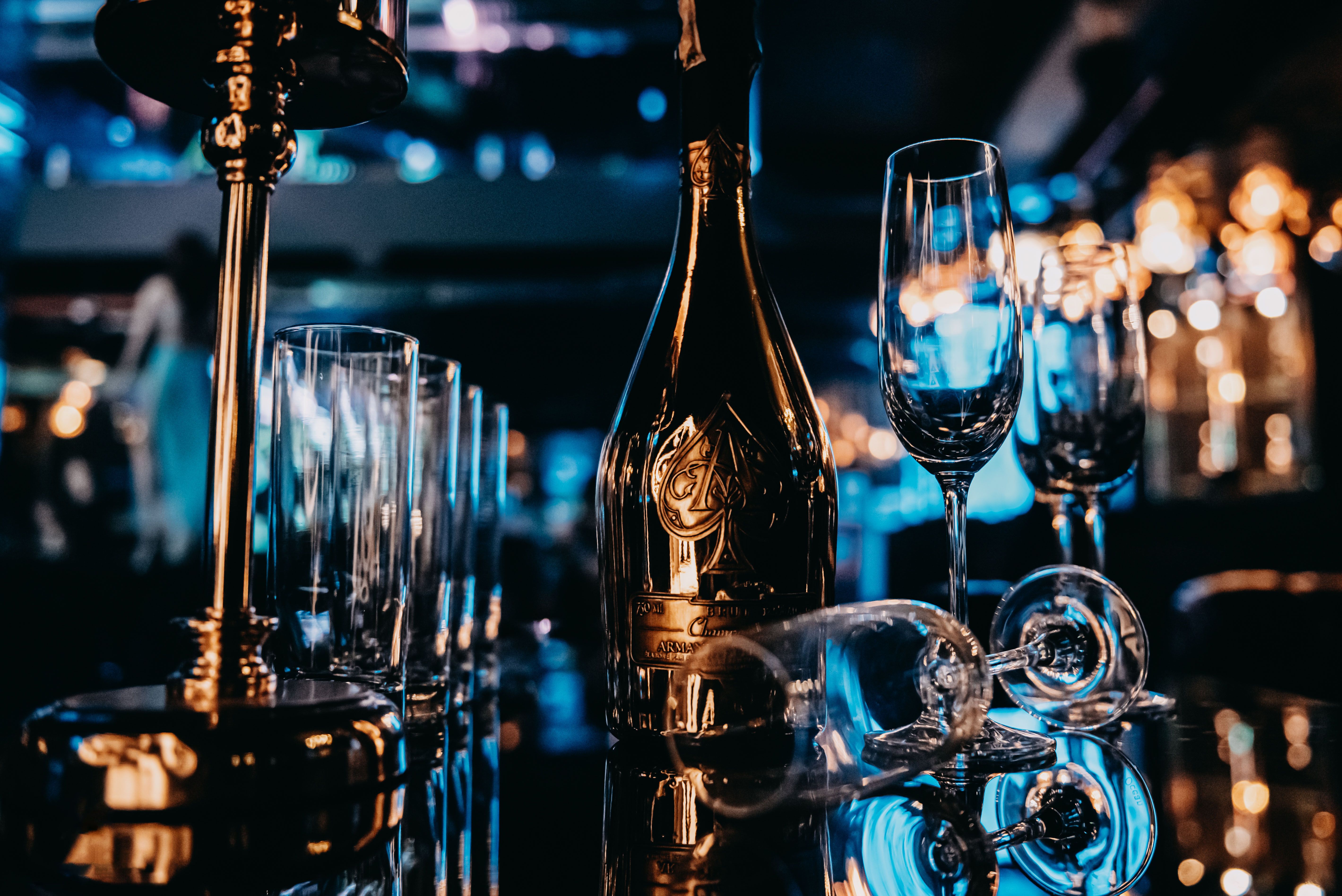 A gold champagne bottle with elegant wine glasses on a reflective surface, exuding luxury