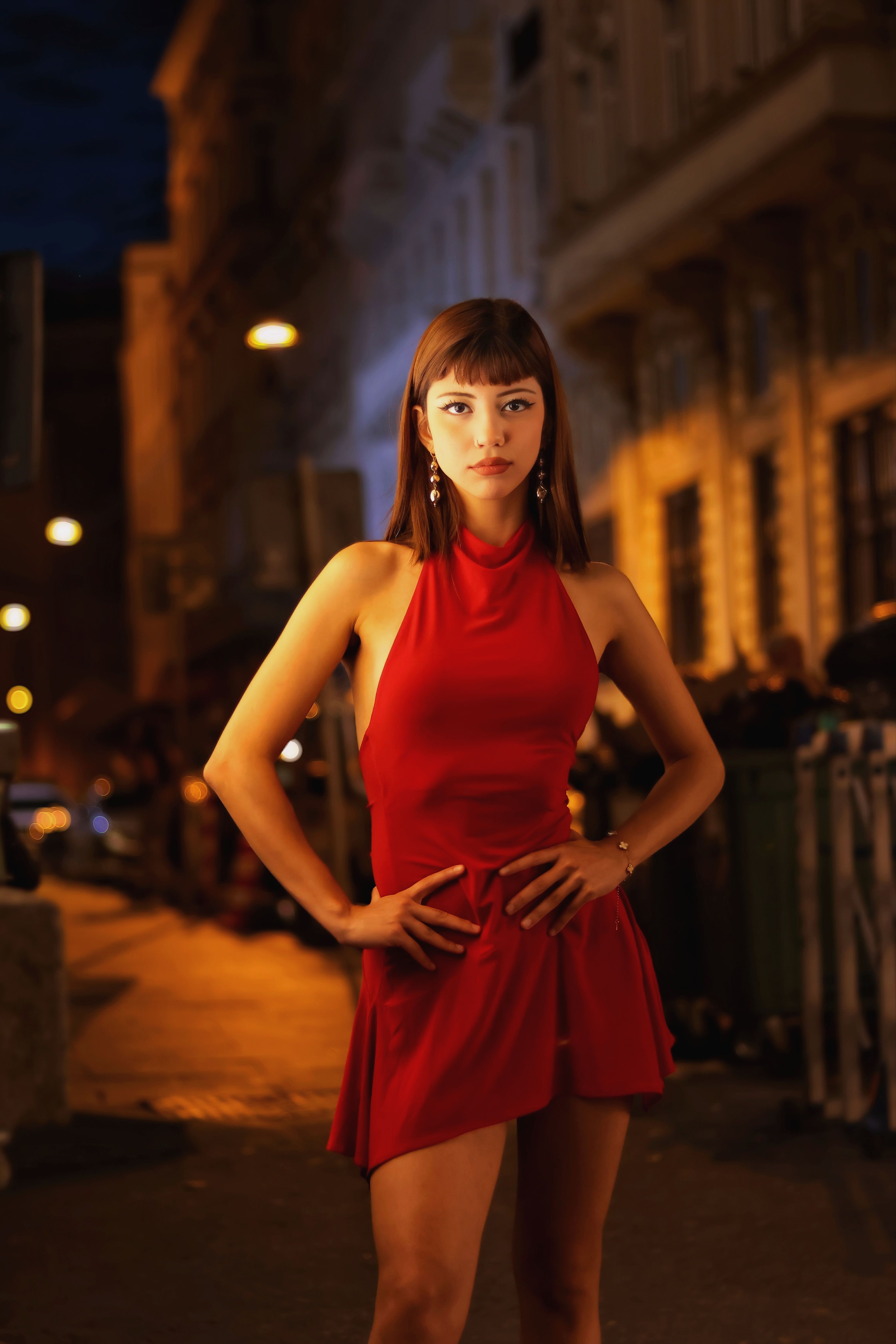 Confident woman in an elegant red dress poses on a vibrant city street at night