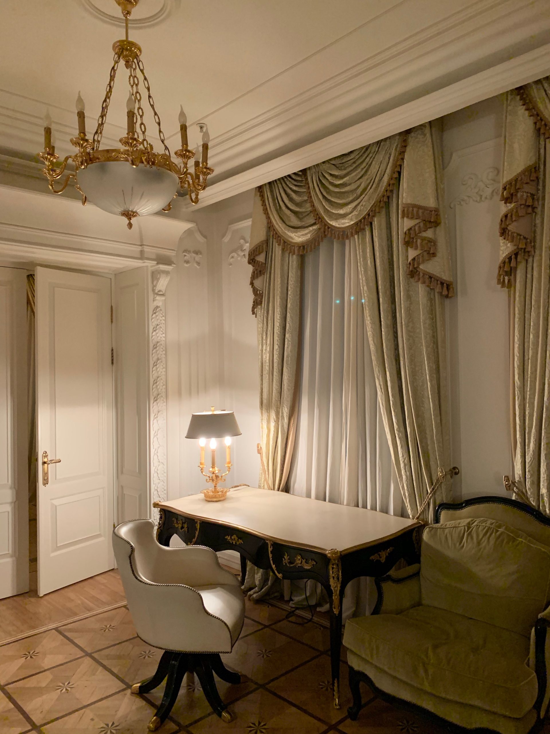 Luxurious hotel room interior featuring a classic chandelier, ornate curtains, and a vintage desk